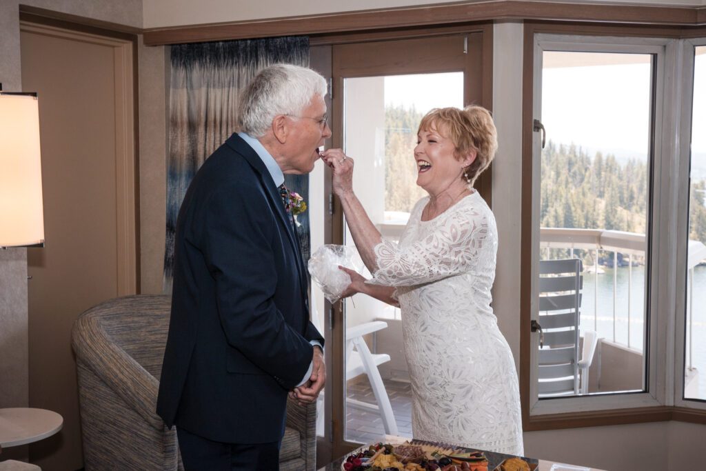 Bride feeding the groom a treat from their celebration spread with laughter.