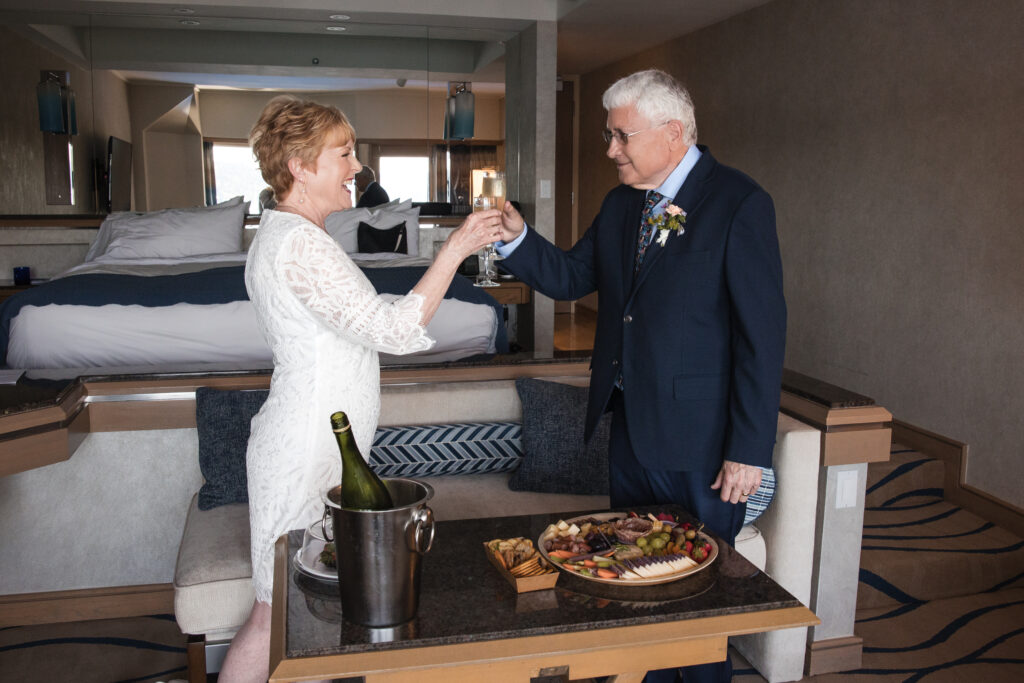 Bride and groom toasting with champagne over a table of snacks and treats.