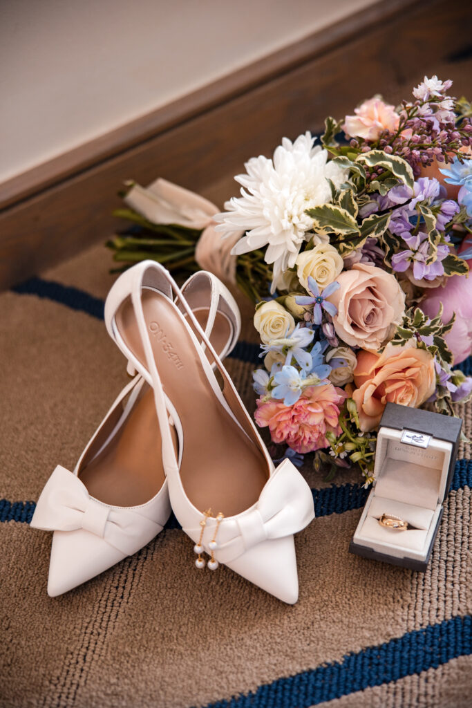 Flat lay of bride’s white shoes, bouquet by Pearl and Tin, and wedding rings