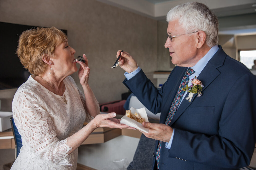 Bride and groom over 60 feed each other cake while laughing during their hotel room elopement in North Idaho.