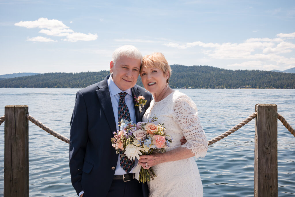 Smiling couple over 60 poses with wedding bouquet beside the lake during their Idaho elopement.