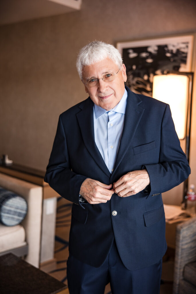 Groom smiling while buttoning navy suit jacket in hotel room