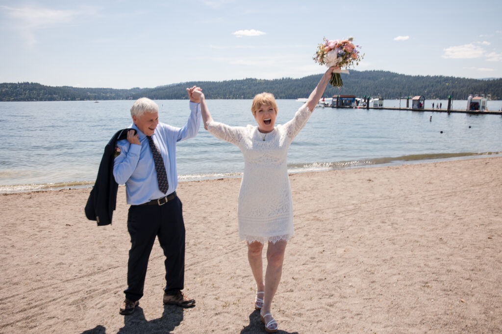 Bride cheering with bouquet in the air during lakeside wedding celebration in Idaho