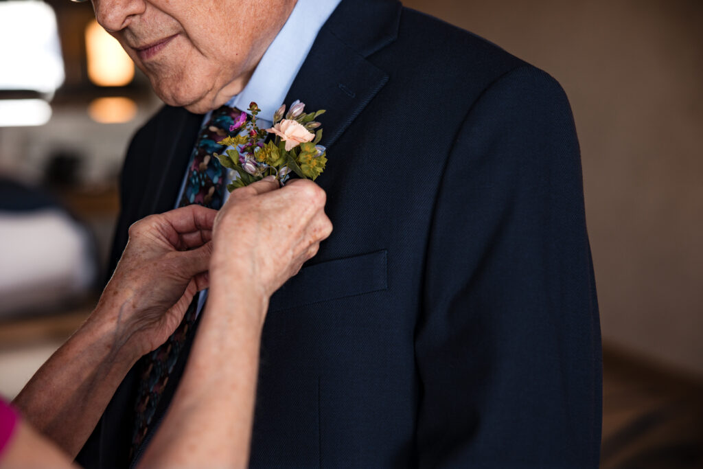 Bride pinning boutonnière with pastel flowers onto groom’s navy lapel