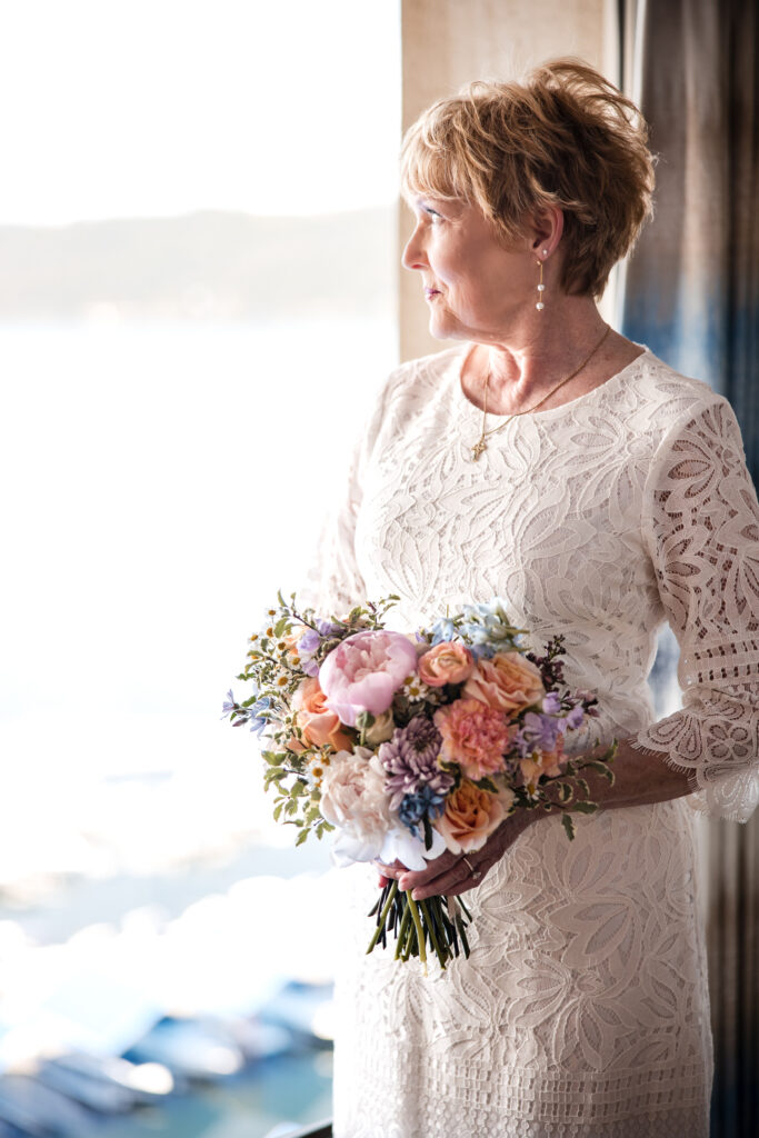 Bride standing by the window with bouquet, overlooking Lake Coeur d’Alene