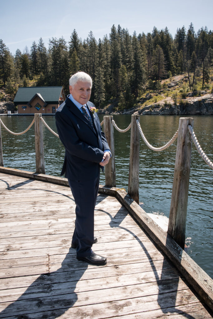 Groom waiting on lakeside dock with trees and cabin in background