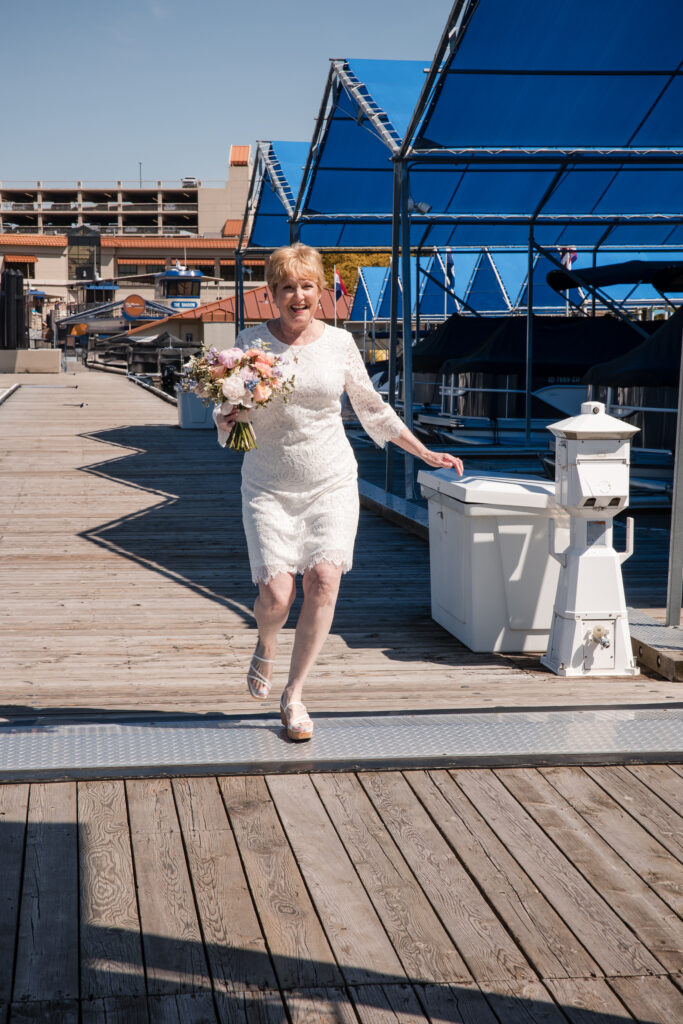 Bride walking quickly down marina dock holding bouquet, smiling