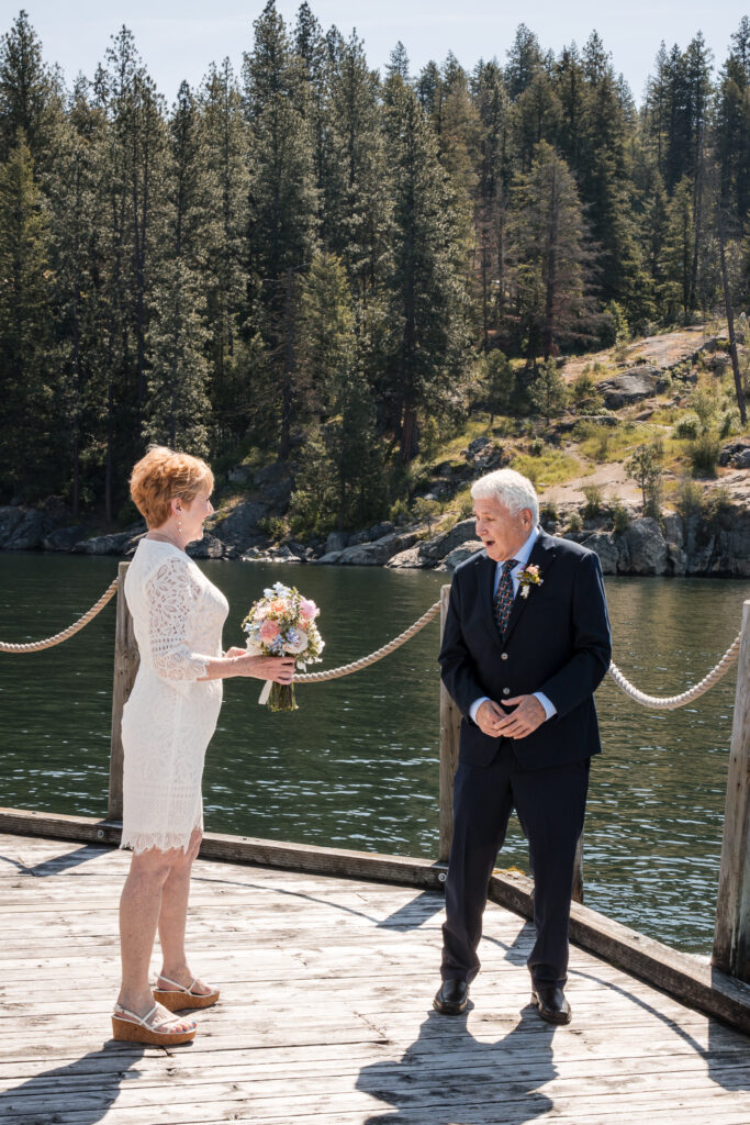 Bride and groom smiling during first look on dock surrounded by water and forest