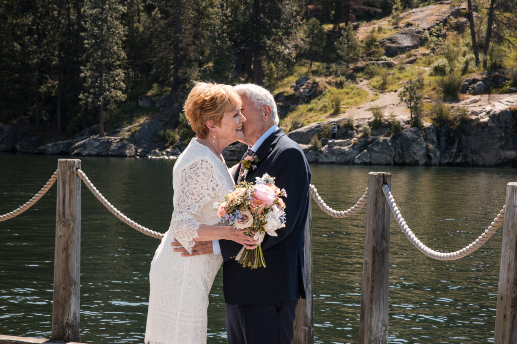 Bride and groom embrace and smile during first look on lakeside dock