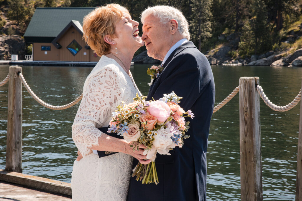 Bride and groom embrace and smile during first look on lakeside dock