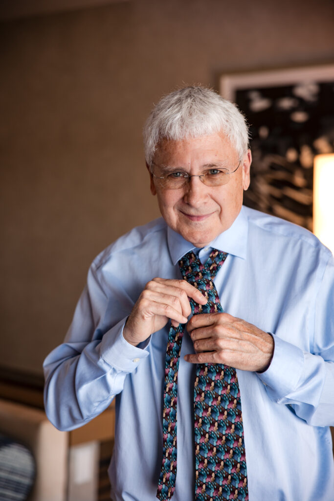 Groom smiling while tying his colorful tie in the hotel room before the ceremony