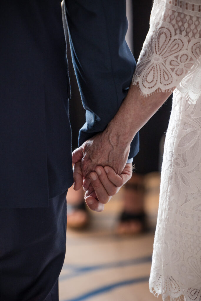 Close-up of couple holding hands during intimate indoor ceremony
