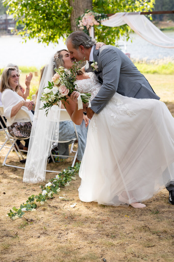 Groom is giving his bride a dip and kiss as guests clap in the background