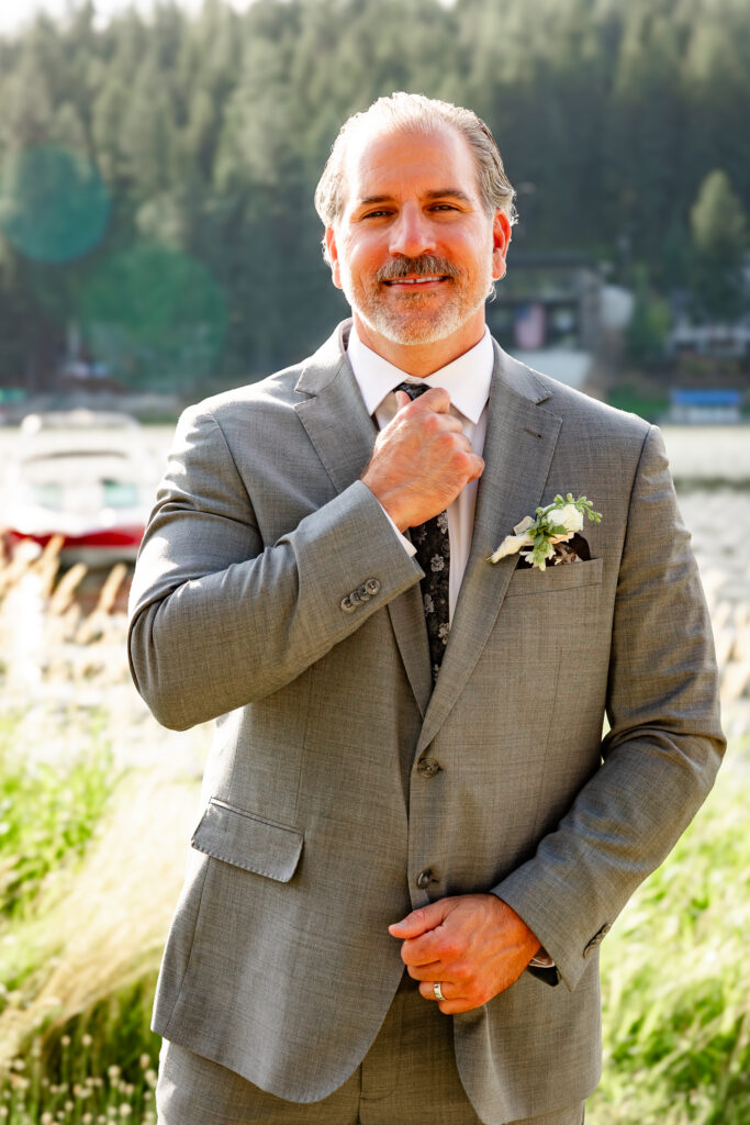 Groom portrait fixing tie by lake