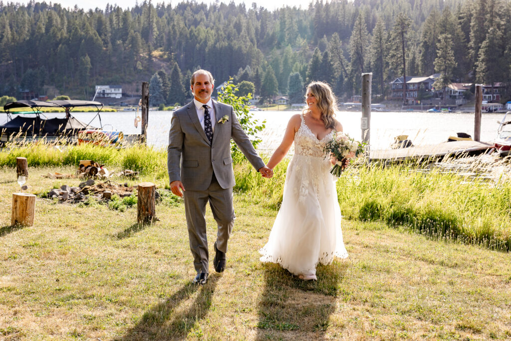The bride and goom walking hand in hand along the lake shore