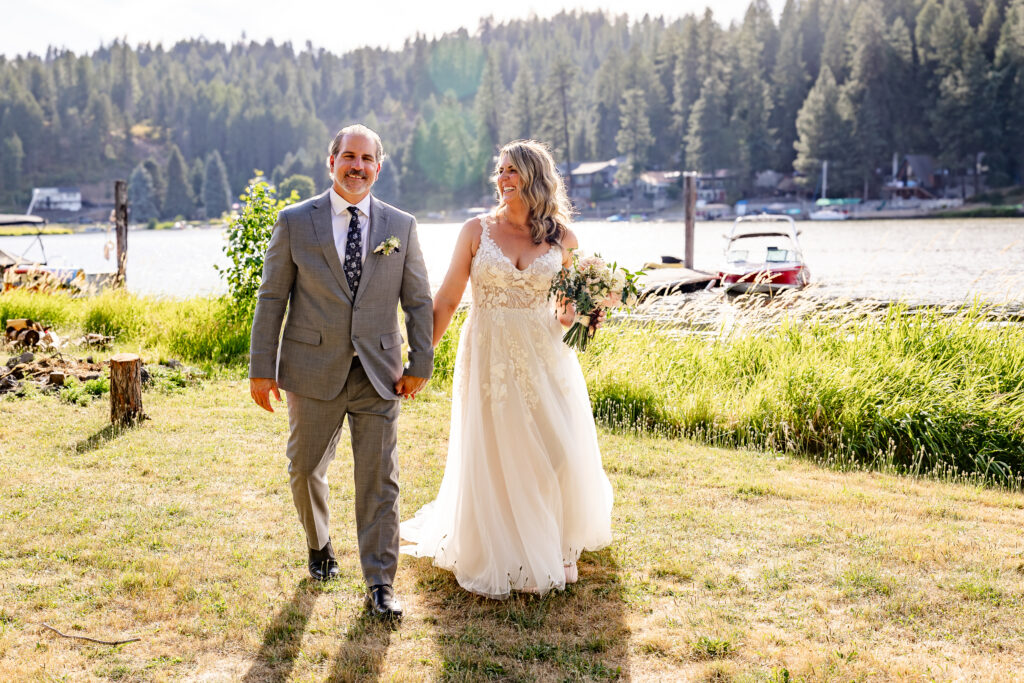 The bride and goom walking hand in hand along the lake shore