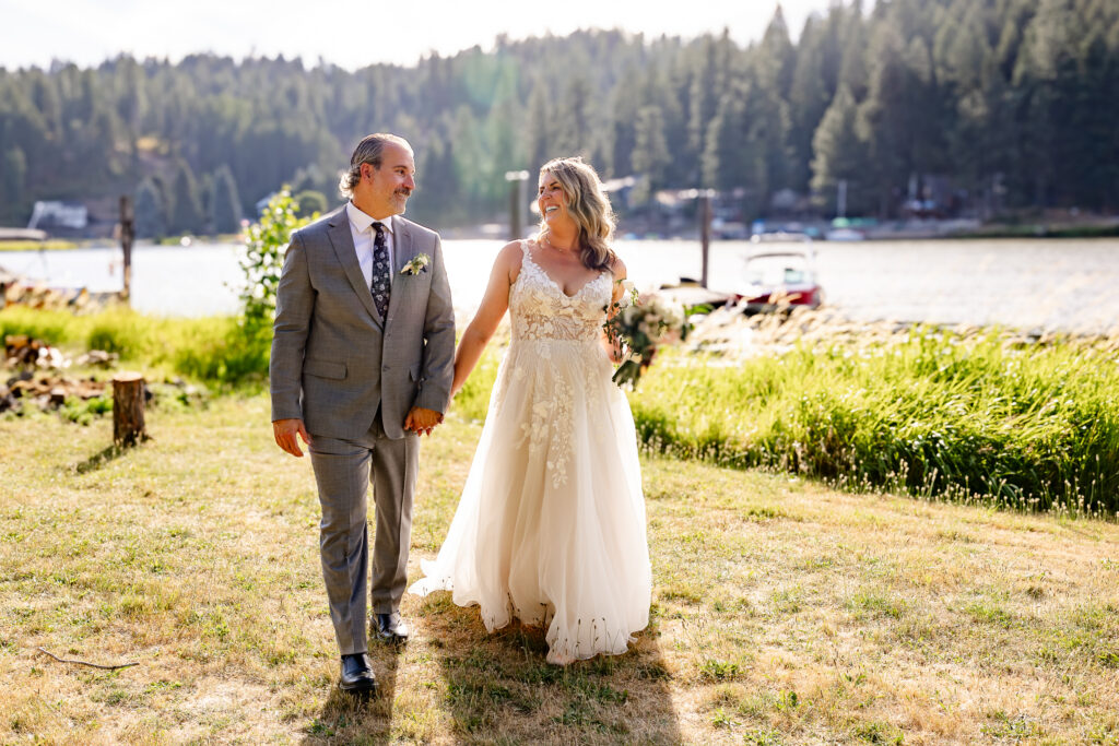 The bride and goom walking hand in hand along the lake shore