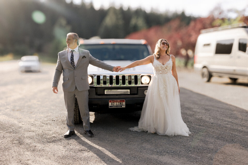 Bride and groom standing in front of limo hands streched apart looking in opposite directions as the suns rays shine across them