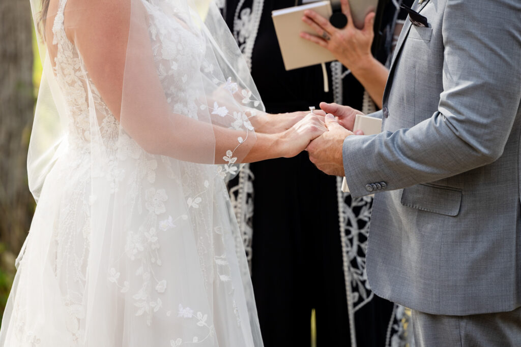 close up of bride and groom holding hands as the officiant performs the ceremony.