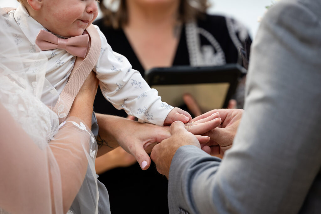Goom placing ring on brides finger while the baby has his hands on hers