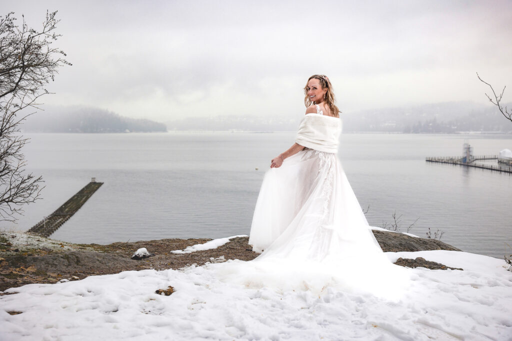 Bride standing on the lake overview looking over shoulder in white wedding dress and warm shawl