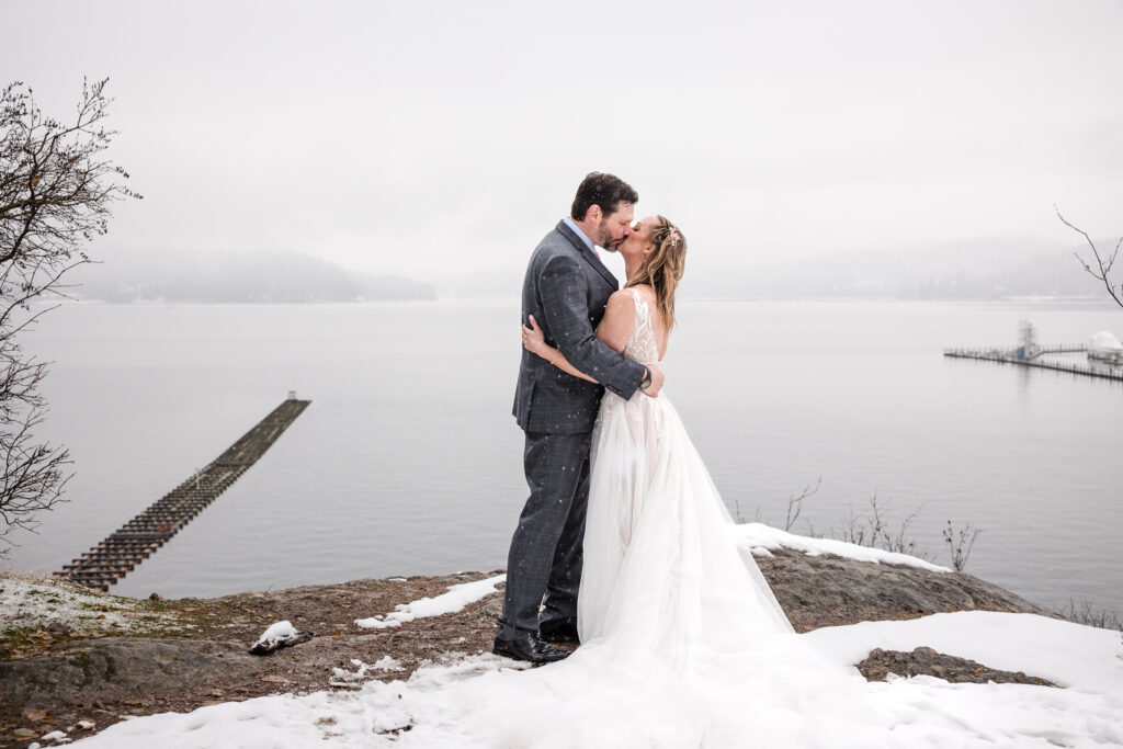 Bride and groom facing each other, kissing overlooking the wintery view of Lake Coeur d'Alene